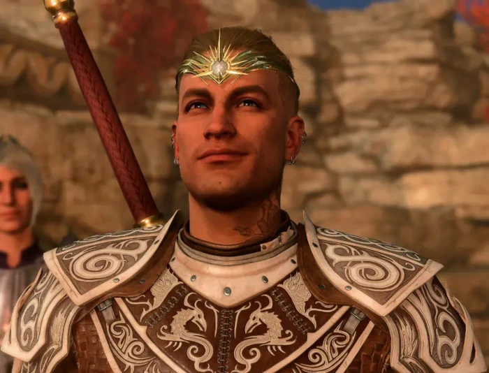 Front and center, a fair-skinned man in white and brown leather armor grins as he looks up and outward with blue eyes. A rose is tattooed on the left side of his neck and both ears have small silver rings. He wears a gold crown on his forehead. The sides of his head are shaved, with his blond hair pulled back.