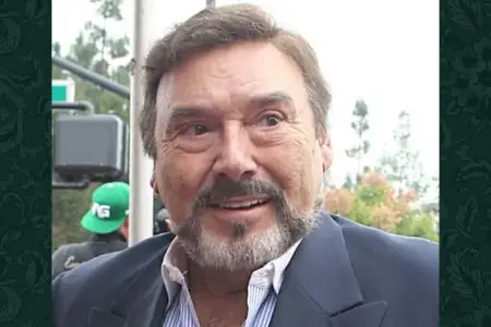 A mature gent with brown hair and eyes and a salt and pepper trimmed beard stands in a dark blue suit and smiles while looking off to the right.